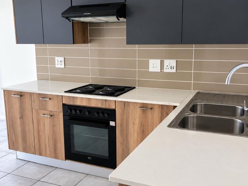 Modern kitchen featuring wood-grain lower cabinetry, matte grey upper cabinets, stone countertops, integrated electric oven and hob, and a double stainless steel sink.