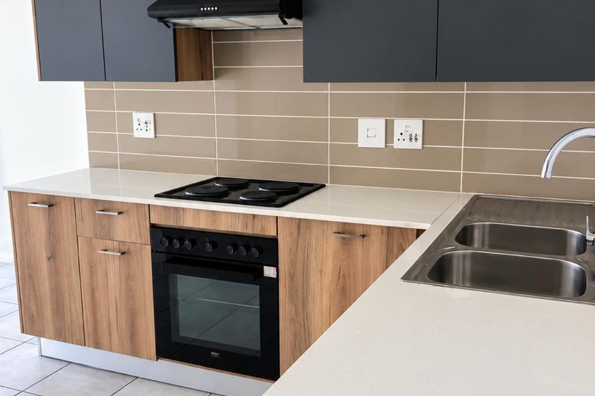 Modern kitchen featuring wood-grain lower cabinetry, matte grey upper cabinets, stone countertops, integrated electric oven and hob, and a double stainless steel sink.