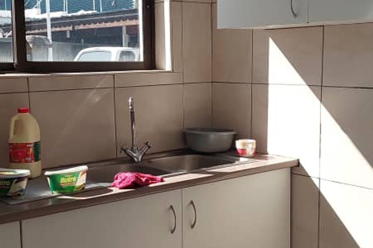 A functional kitchenette area featuring tiled walls, built-in cabinetry, a stainless steel sink, and a window providing natural light.