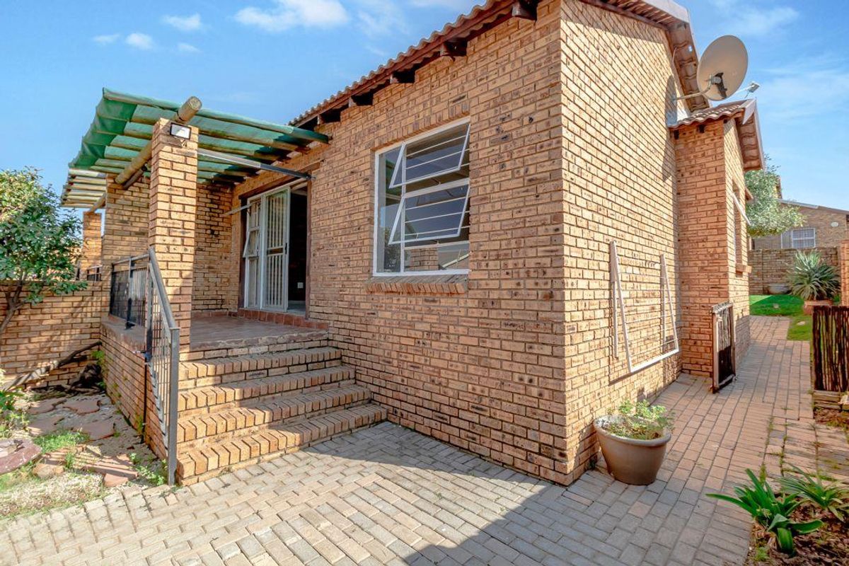 Rear view of the townhouse featuring a face-brick facade, a raised patio area with a pergola, and paved outdoor space.