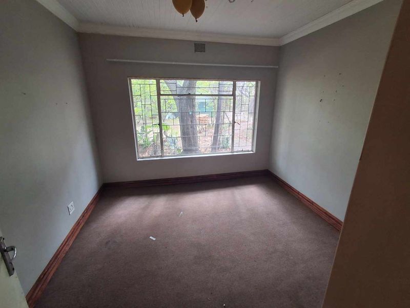 An empty bedroom featuring carpet flooring, timber skirting boards, and security bars on the window, offering a blank canvas for renovation.