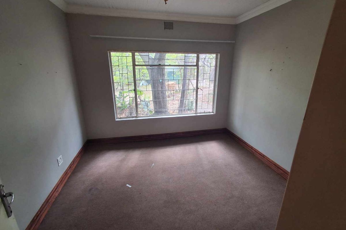 An empty bedroom featuring carpet flooring, timber skirting boards, and security bars on the window, offering a blank canvas for renovation.
