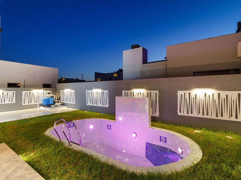 A well-maintained outdoor pool area featuring a small swimming pool with integrated lighting, decorative wall panels, and a clean lawn.
