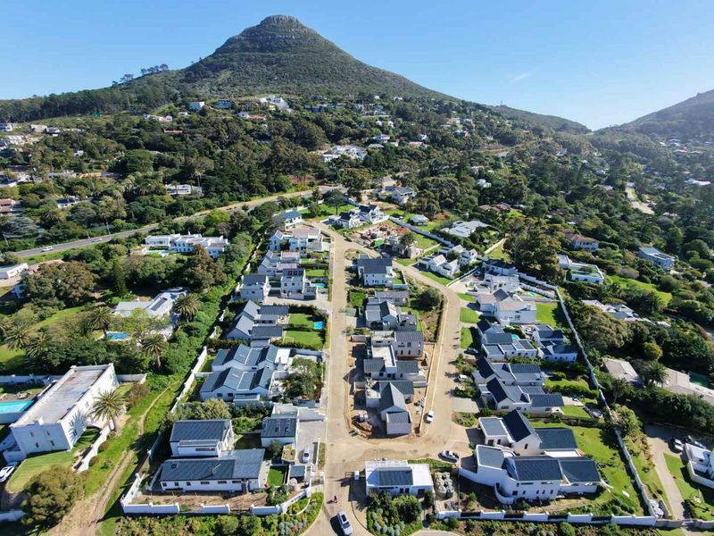 An aerial view of a residential estate featuring multiple homes, paved streets, and landscaped gardens set against a mountain backdrop.