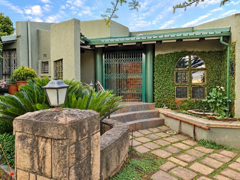 Front entrance featuring a stone masonry wall, paved walkway, security gate, and climbing greenery on the exterior facade.
