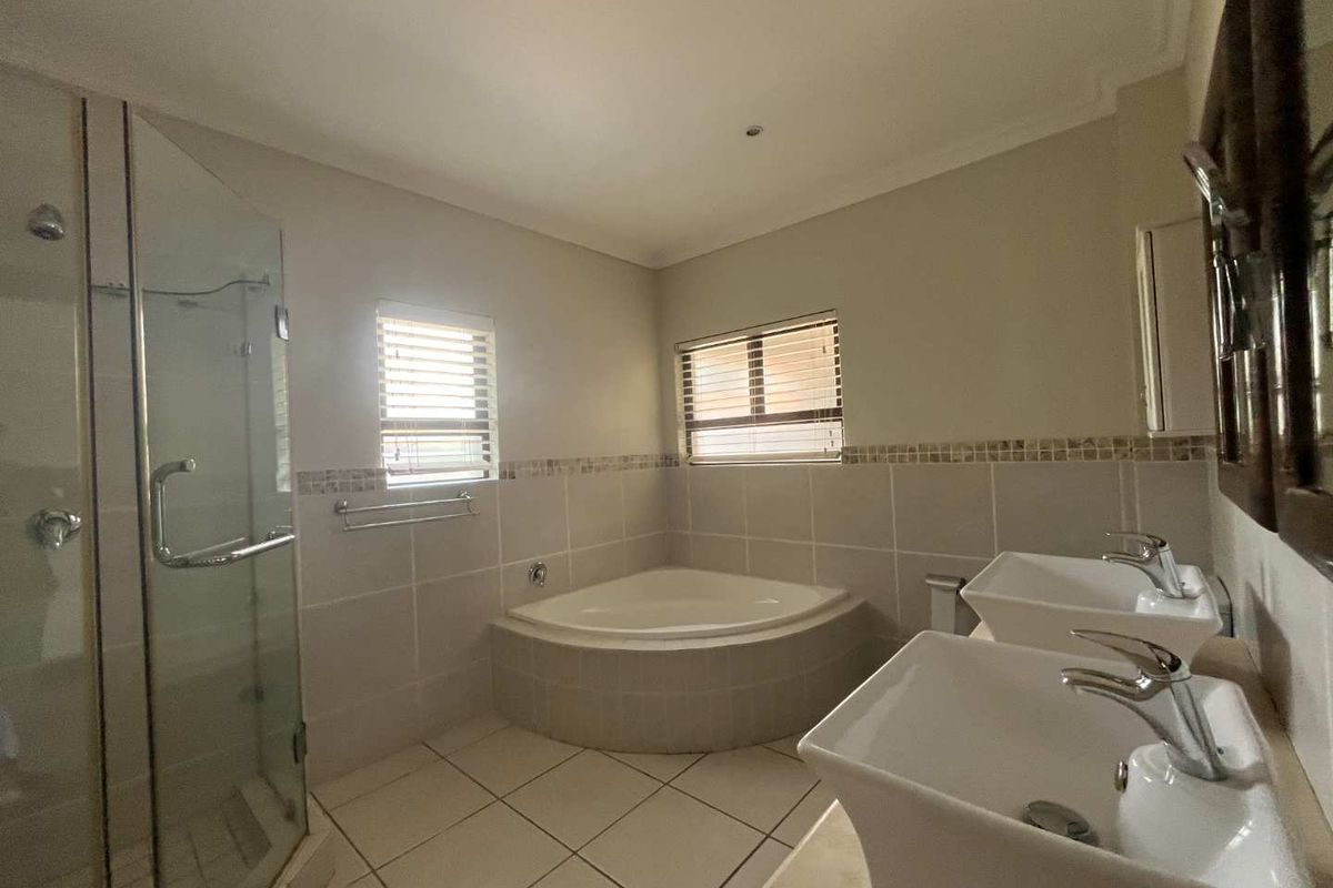 A functional bathroom featuring a corner bathtub, a glass-enclosed shower, and dual vessel sinks set on a vanity.