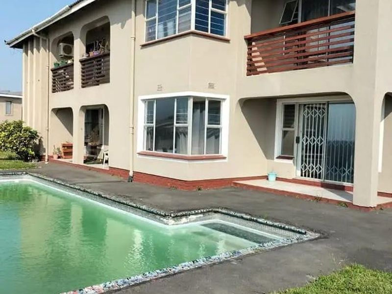 Rear view of a two-story residential building featuring multiple balconies, sliding glass doors with security gates, and an adjacent swimming pool.