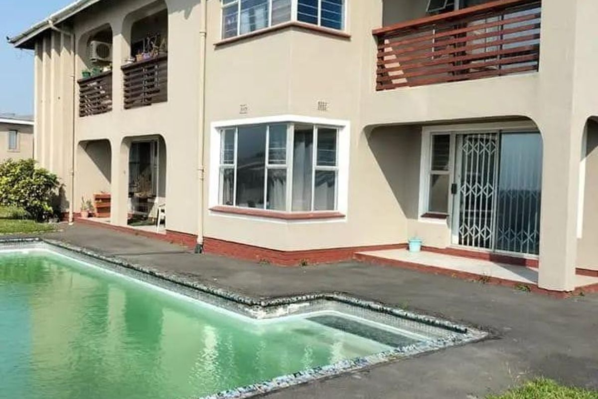 Rear view of a two-story residential building featuring multiple balconies, sliding glass doors with security gates, and an adjacent swimming pool.