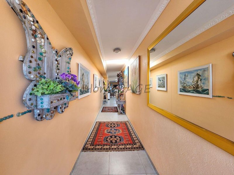 A long residential hallway featuring tiled flooring, crown molding, and warm-toned wall finishes, providing access to various rooms within the home.