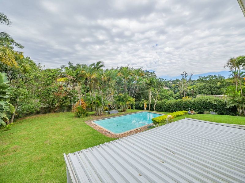 A private backyard featuring a swimming pool with stone coping, surrounded by a lush garden and a covered patio area.