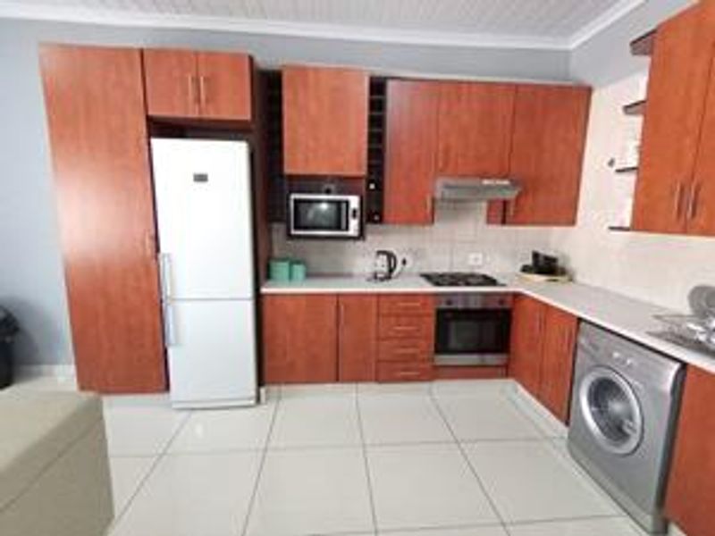 Functional kitchen featuring warm-toned cabinetry, integrated appliances including an oven and hob, tiled flooring, and a practical layout with ample storage space.