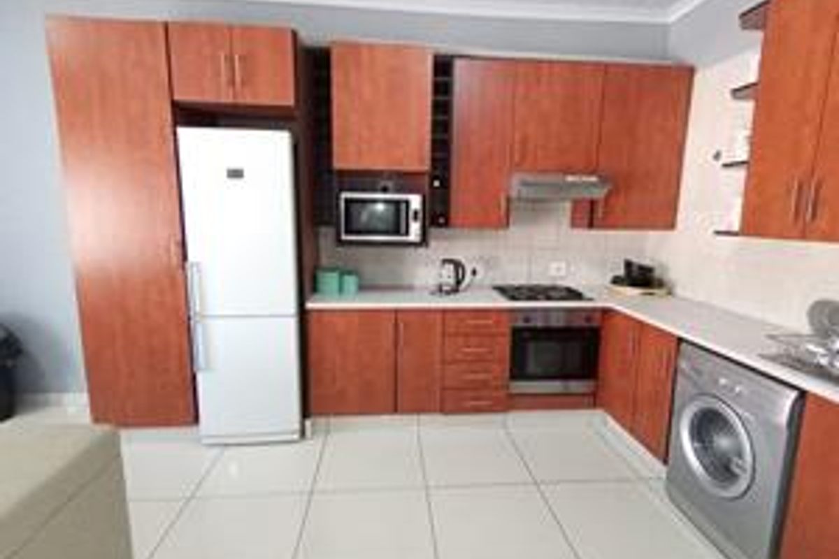 Functional kitchen featuring warm-toned cabinetry, integrated appliances including an oven and hob, tiled flooring, and a practical layout with ample storage space.