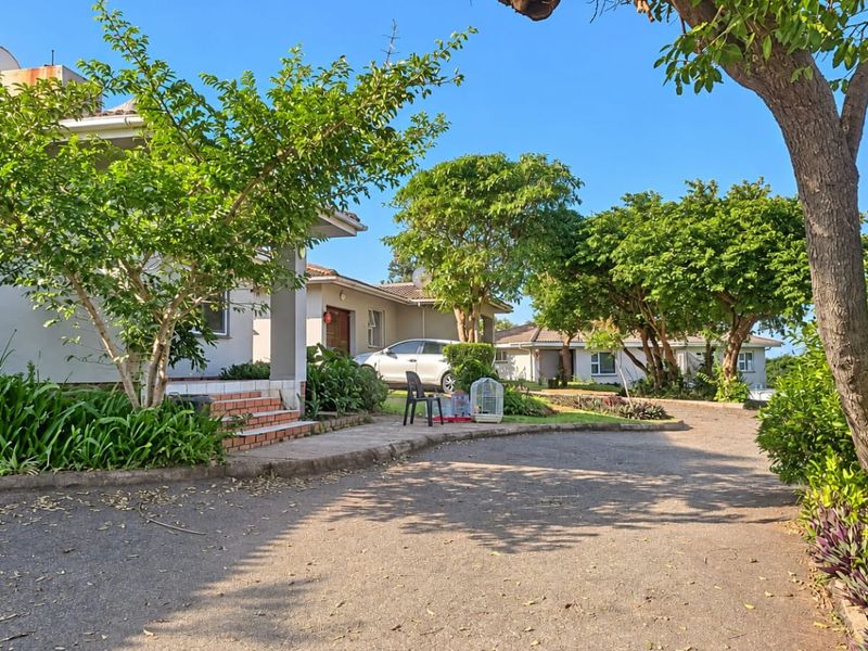 A view of the front exterior of the cluster property, featuring a paved driveway, landscaped garden area, and traditional building facade.