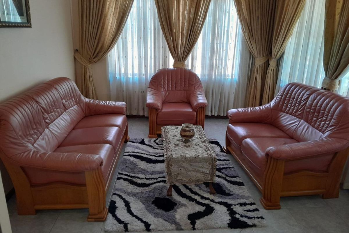 A living room featuring tiled flooring and large windows dressed with floor-to-ceiling curtains.