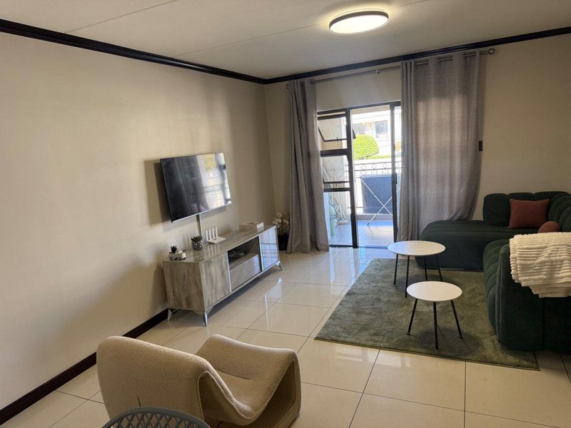 A well-maintained living room featuring large format floor tiles, coving, and a sliding glass door providing access to an outdoor balcony area.