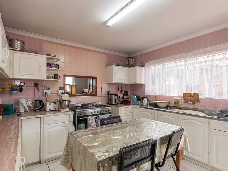 A functional kitchen featuring white built-in cabinetry, a gas stove with oven, and a stainless steel sink, finished with pink wall tiling.