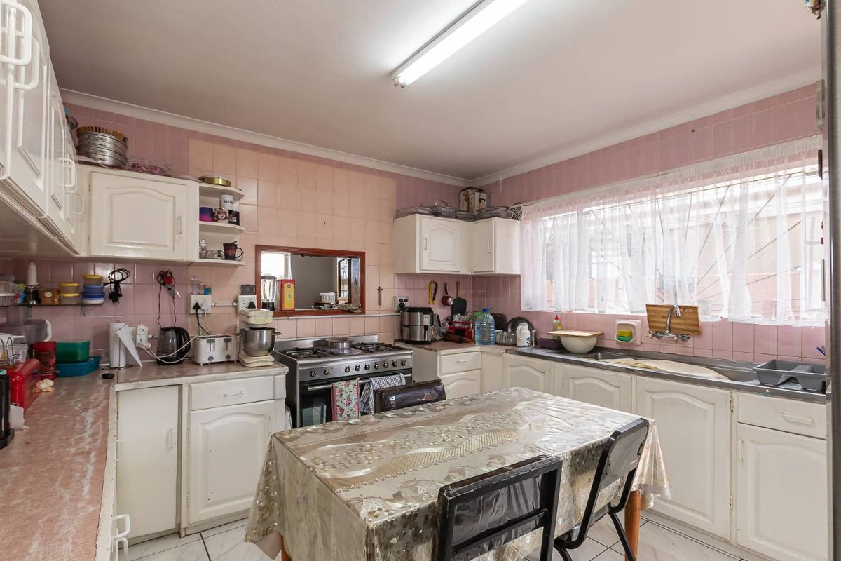 A functional kitchen featuring white built-in cabinetry, a gas stove with oven, and a stainless steel sink, finished with pink wall tiling.