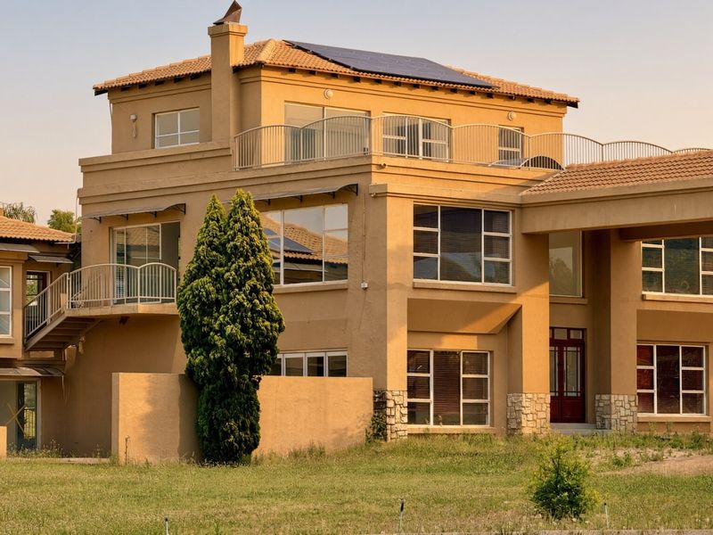 Rear elevation of a multi-story residential property featuring a tiled roof, solar panels, balconies with metal railings, and stone cladding accents.