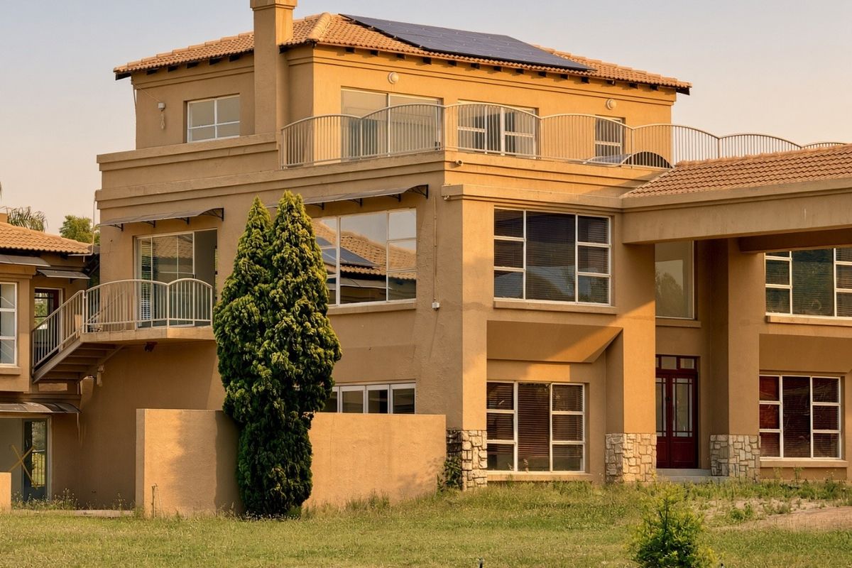 Rear elevation of a multi-story residential property featuring a tiled roof, solar panels, balconies with metal railings, and stone cladding accents.
