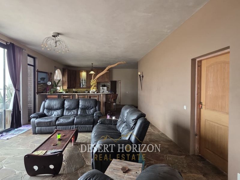 Spacious open-plan living area featuring natural stone flooring and an integrated kitchen with wooden cabinetry and a breakfast bar.