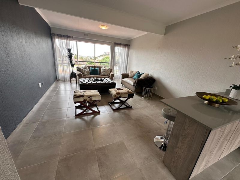 Spacious open-plan living area featuring large sliding glass doors, neutral tiled flooring, and a modern kitchen island, offering a bright and functional layout.