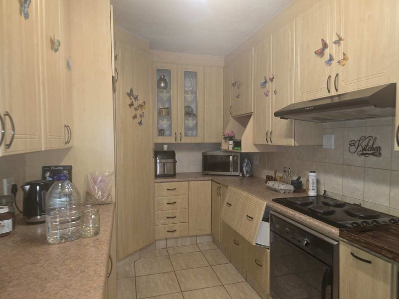 A functional kitchen featuring light wood-finish cabinetry, laminate countertops, built-in oven, electric hob, and tiled flooring with a tiled backsplash.