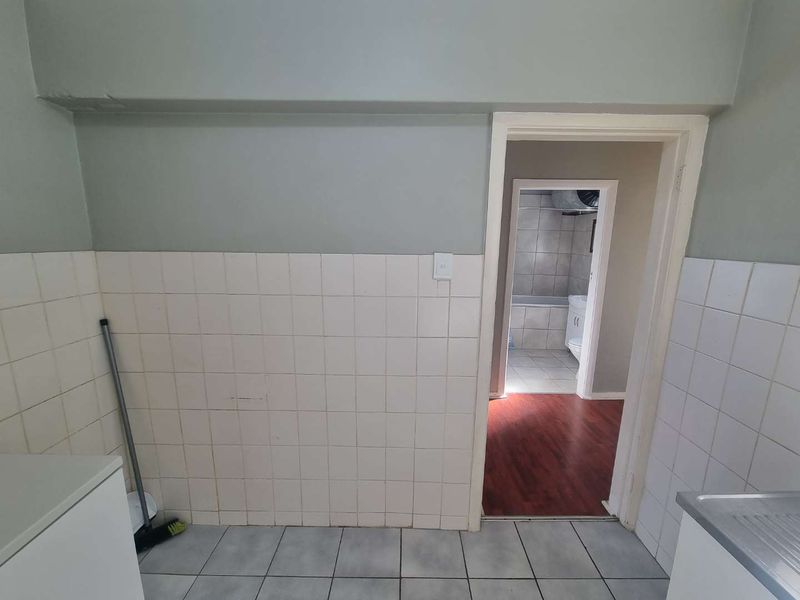 A functional kitchen area featuring tiled splashbacks and flooring, with a clear view through to an adjacent bathroom space.