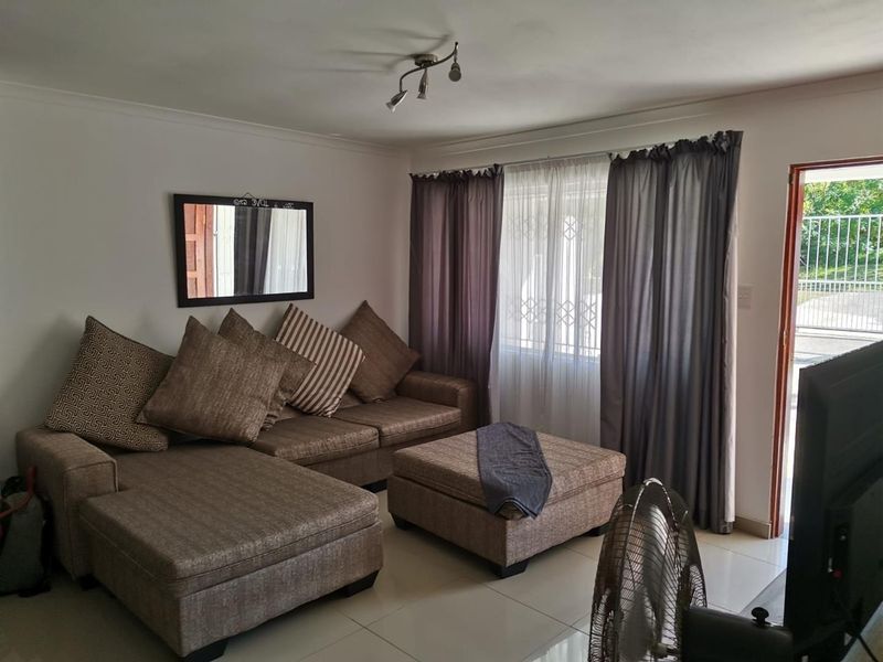 A comfortable living room featuring tiled flooring, neutral wall finishes, and direct access to the exterior through a security-fitted door.