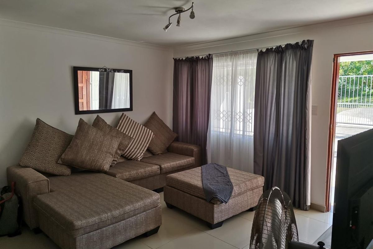 A comfortable living room featuring tiled flooring, neutral wall finishes, and direct access to the exterior through a security-fitted door.