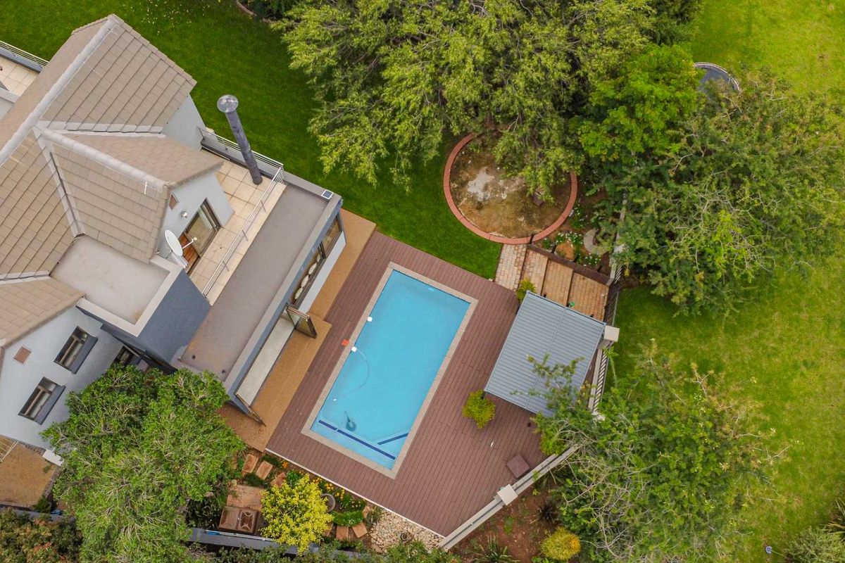 Aerial view of the property featuring a swimming pool, wooden decking, a covered patio area, and a spacious landscaped garden.