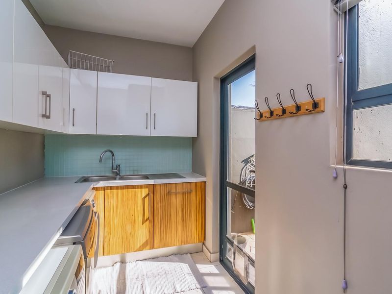 A compact and functional scullery featuring modern white and wood-grain cabinetry, a stainless steel sink, and direct access to an outdoor area.