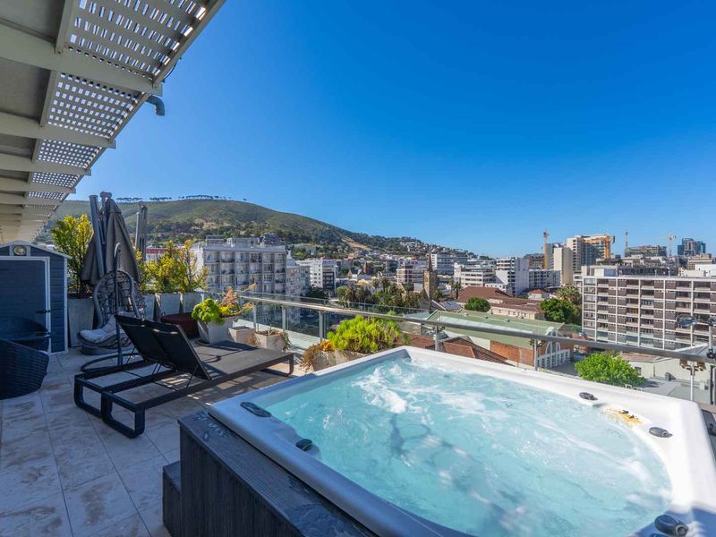 Spacious penthouse balcony featuring a built-in hot tub, glass balustrade, and expansive city and mountain views.