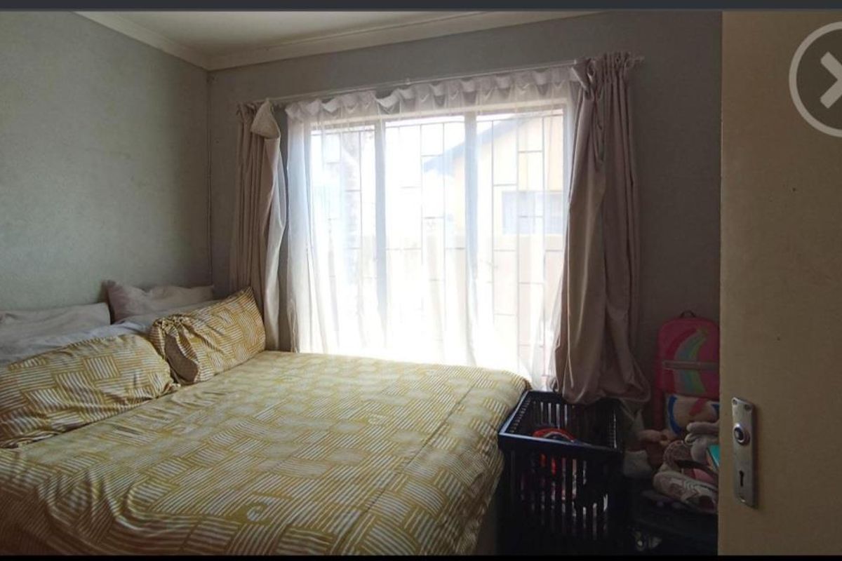 A functional bedroom featuring a large window with security bars and neutral wall finishes.