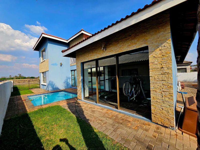 Rear exterior view featuring a swimming pool, paved patio area, and stone-clad wall with large sliding glass doors leading into the home.