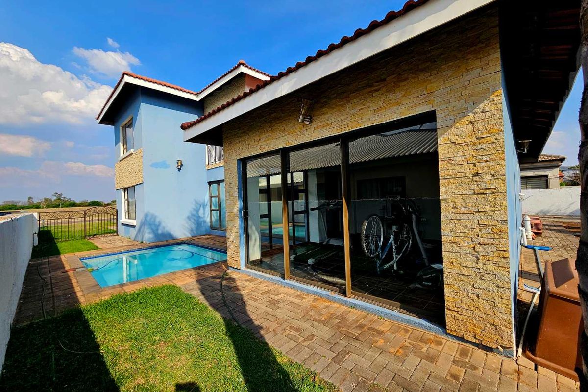 Rear exterior view featuring a swimming pool, paved patio area, and stone-clad wall with large sliding glass doors leading into the home.
