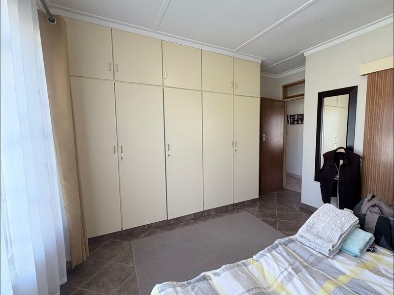 A bedroom featuring extensive built-in cupboards, tiled flooring, and neutral wall finishes, offering practical storage and a functional layout.