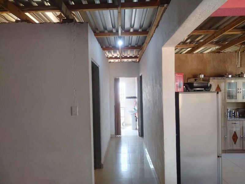 A hallway leading to a bathroom, featuring tiled floors and an unfinished exposed timber and corrugated metal ceiling structure.