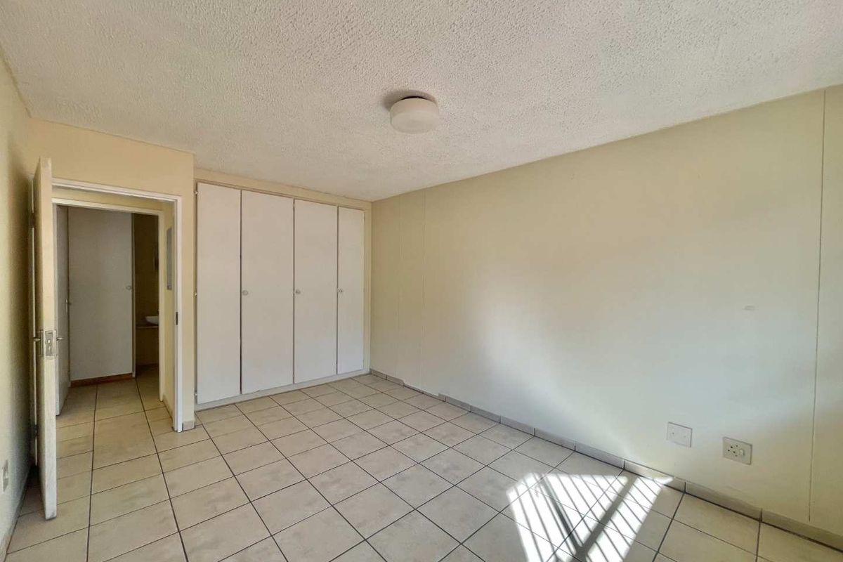 An empty bedroom featuring tiled flooring and built-in cupboards, offering a blank canvas for personalization.