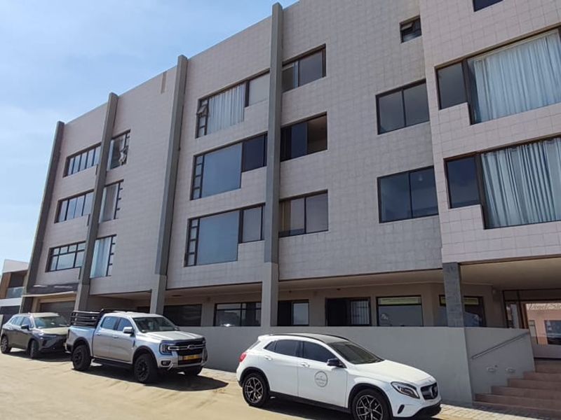 A modern multi-story apartment building featuring a tiled facade, large windows, and a paved entrance area with concrete steps.