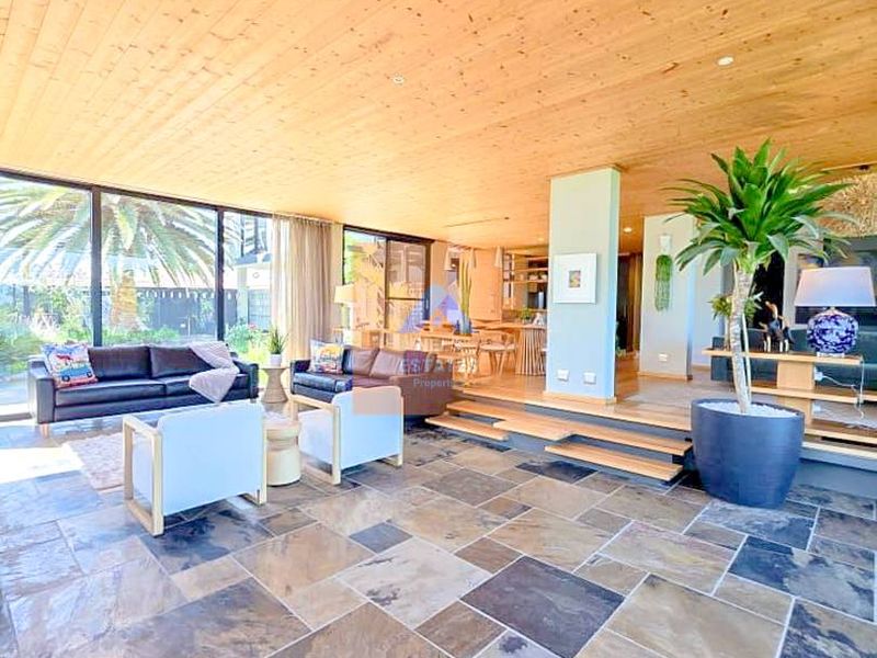 Spacious open-plan living area featuring a warm timber-clad ceiling, natural stone flooring, and expansive floor-to-ceiling glass doors that provide seamless indoor-outdoor flow.