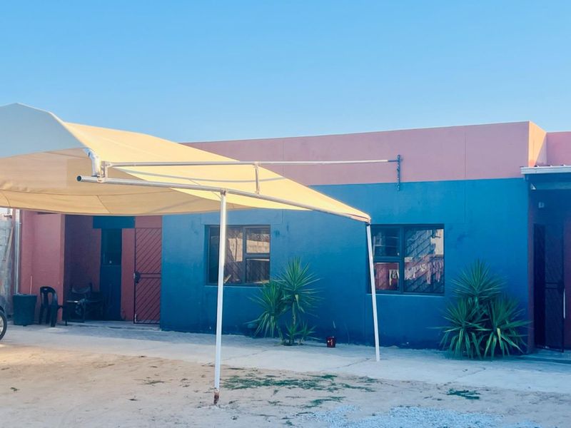 Rear exterior view of the apartment featuring a shade sail, concrete paving, and security gates on the building access points.