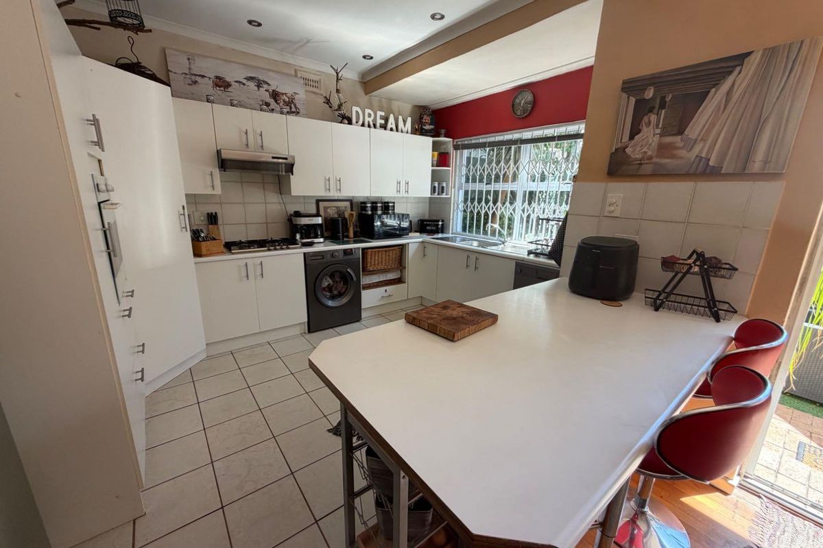 Functional kitchen featuring white cabinetry, tiled flooring, integrated gas hob, extractor fan, and a breakfast counter with direct access to the outdoor area.