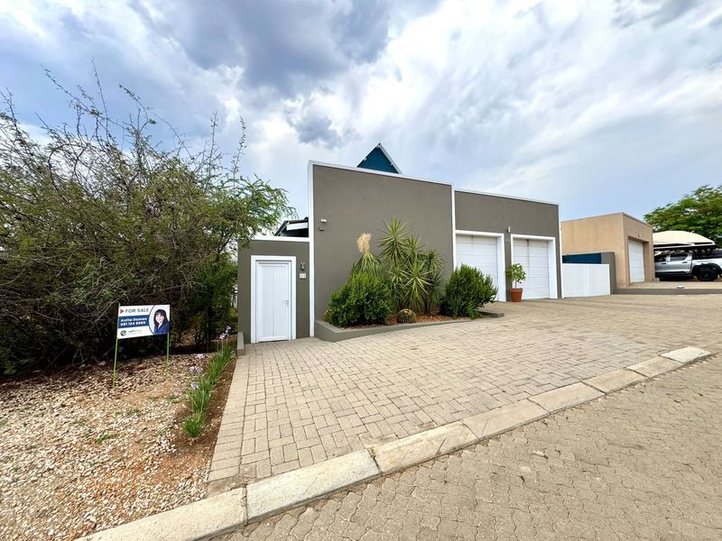 Front elevation of a modern house featuring a paved driveway, double garage doors, and a private pedestrian entrance with established garden landscaping.
