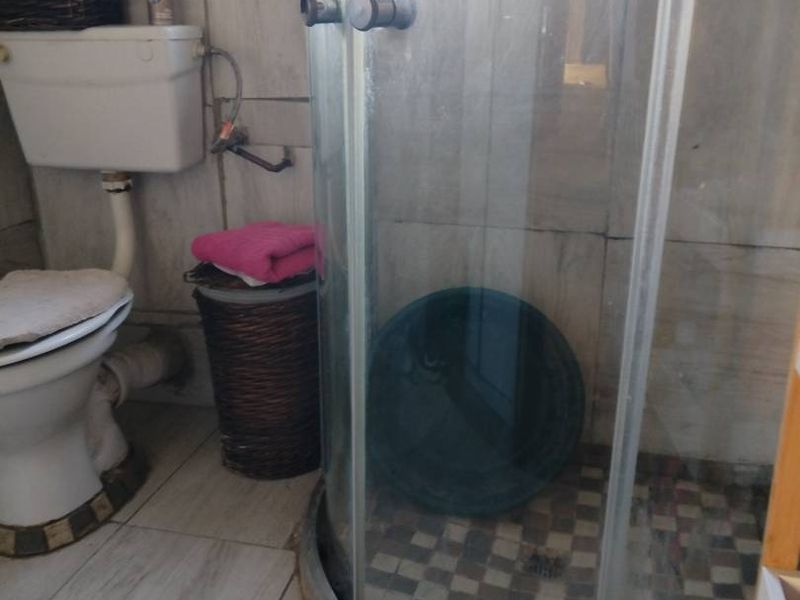 A compact bathroom featuring a corner shower enclosure and standard toilet with tiled finishes throughout.