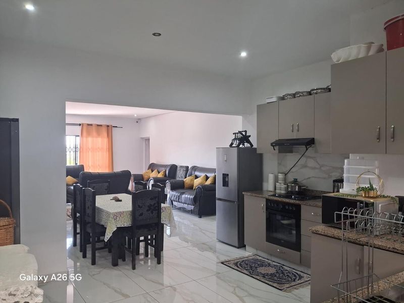 Open-plan living and kitchen area featuring modern cabinetry, granite countertops, built-in oven, hob, and polished tiled flooring throughout the space.