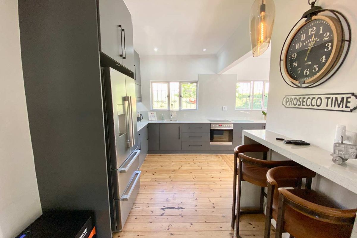 Modern kitchen featuring dark grey cabinetry, integrated stainless steel appliances, stone countertops, and a breakfast bar with timber flooring.