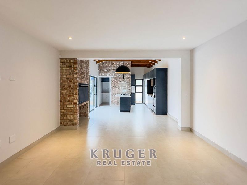 Spacious open-plan living and kitchen area featuring exposed brick accents, timber ceiling beams, modern cabinetry, and a central kitchen island.