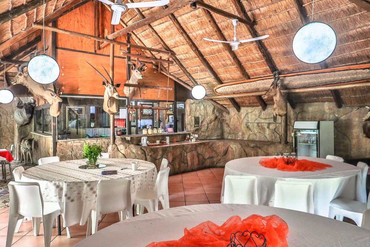 Spacious rustic entertainment area featuring a high thatched roof, exposed timber beams, stone-clad walls, and a built-in service counter.