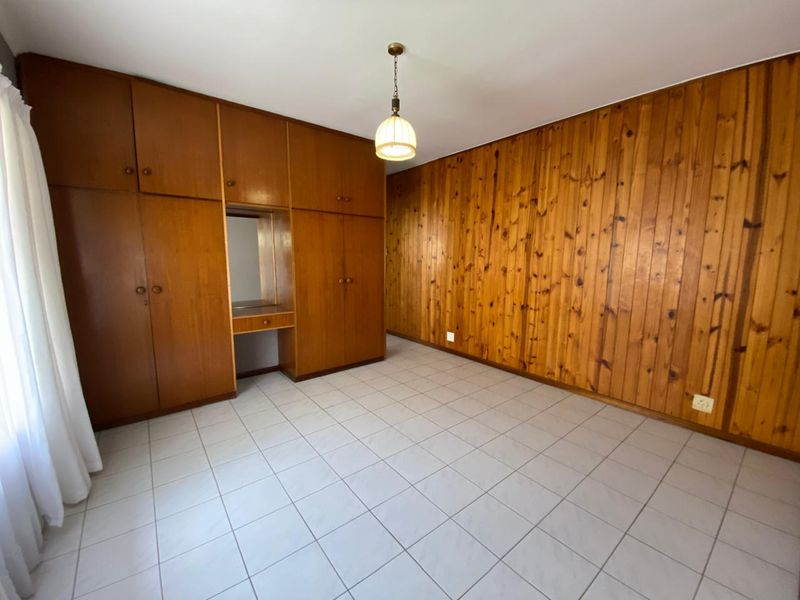 A spacious bedroom featuring built-in wooden cupboards, classic wood paneling on the walls, and neutral tiled flooring throughout.