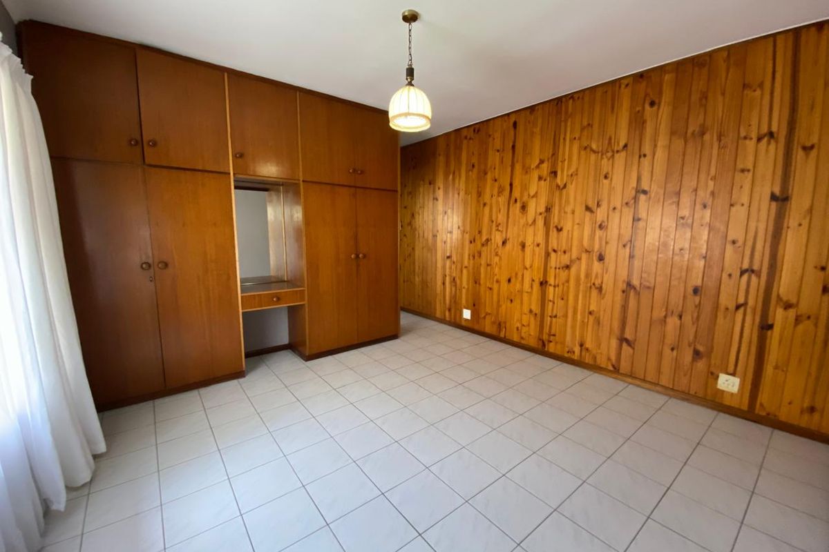 A spacious bedroom featuring built-in wooden cupboards, classic wood paneling on the walls, and neutral tiled flooring throughout.
